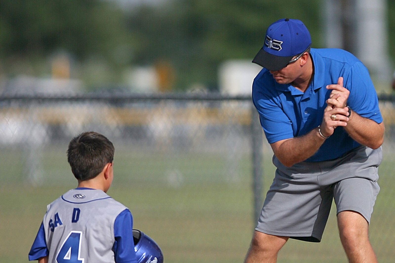 Youth baseball coach demonstrating a hand position to a young player kneeling on the infield during practice