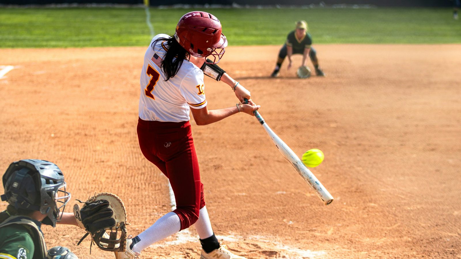 A softball hitter driving through a yellow softball at contact, filmed from the side