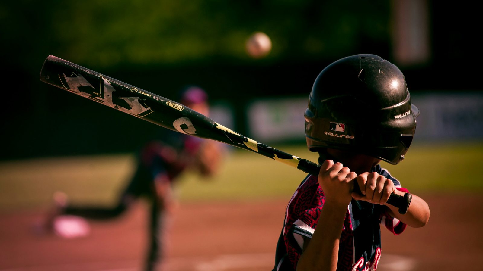 A youth hitter with both hands on the bat knob as the pitch comes in