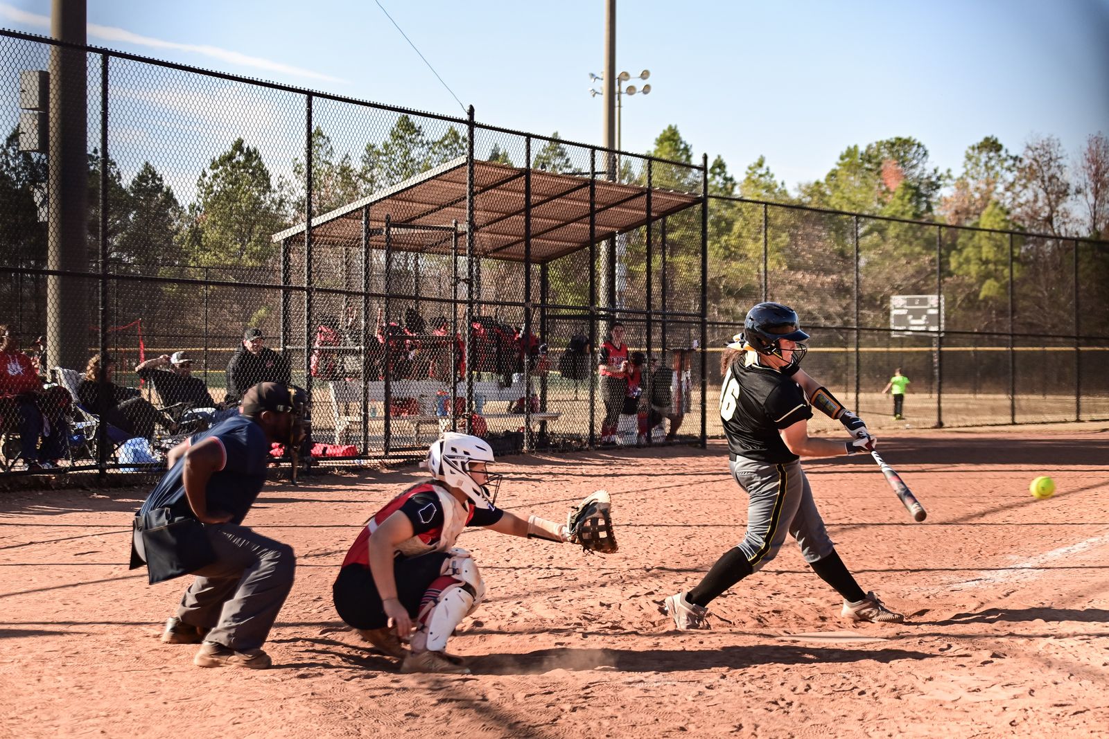 Fastpitch softball hitter mid-swing as the ball arrives, catcher and umpire behind the plate