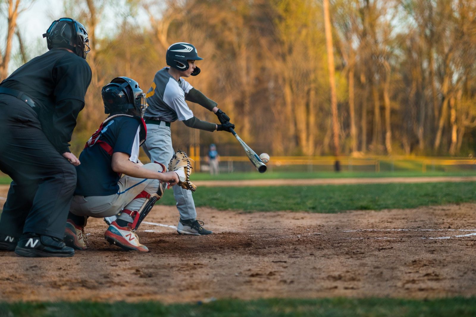 Youth hitter making compact contact on a pitch away, catcher and umpire behind the plate