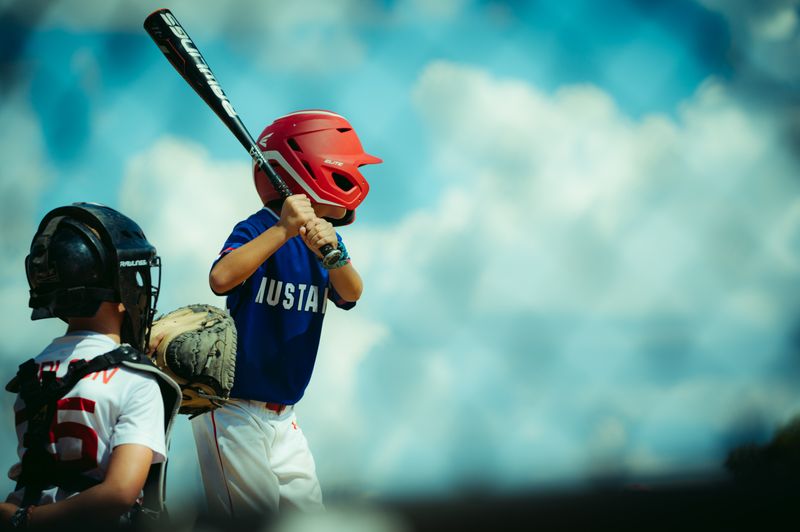 Youth batter in a helmet lining up a swing against a cloudy sky