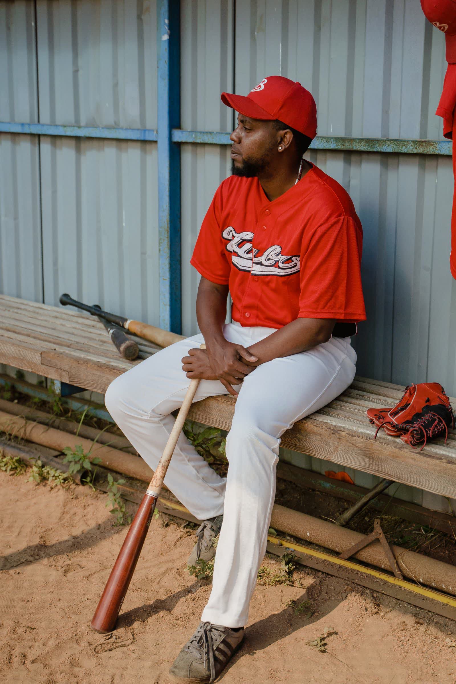 Young player sitting alone on the dugout bench with a bat across his knees